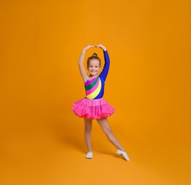 Photo of Cute little girl in costume dancing on orange background