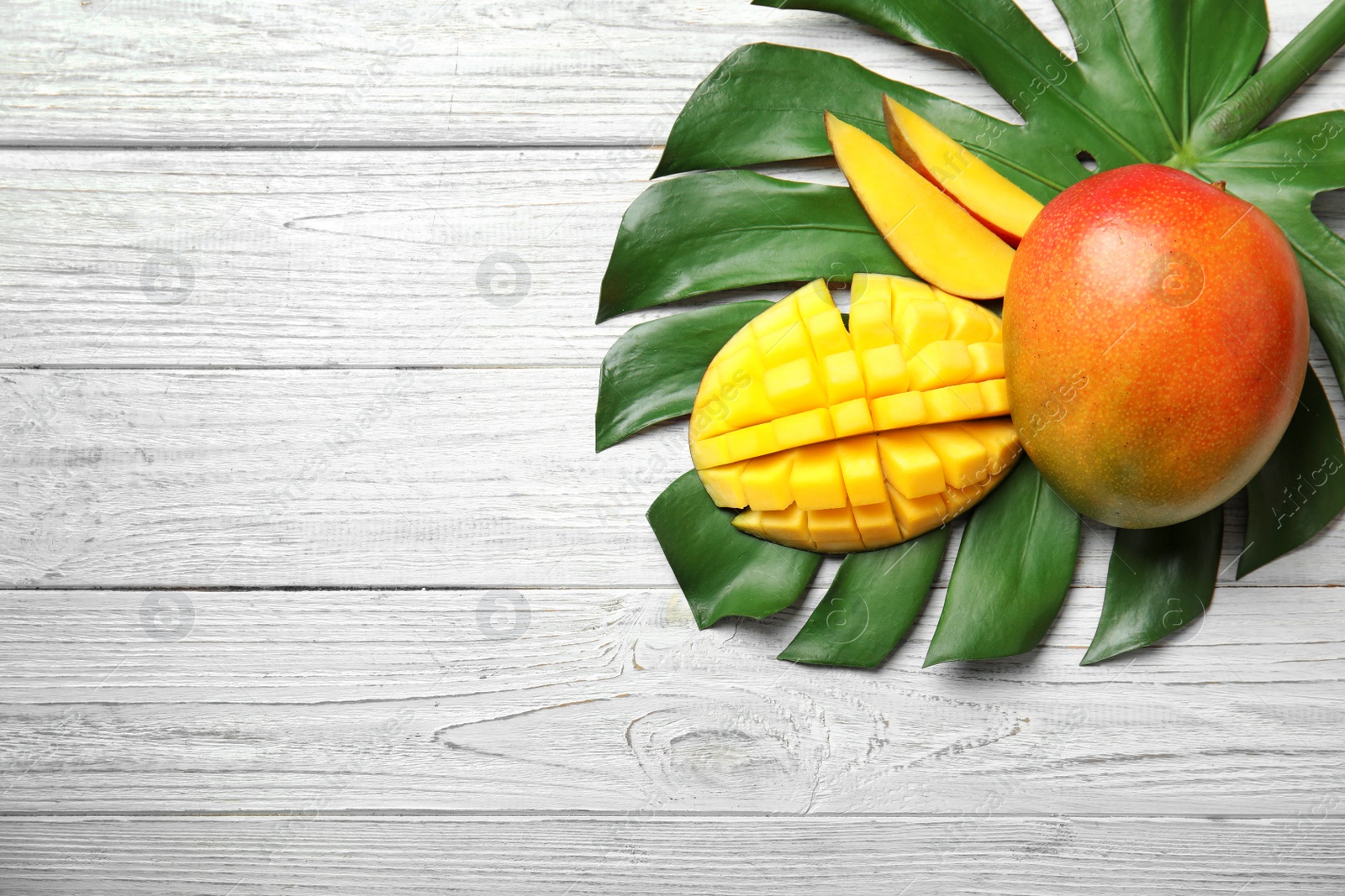 Photo of Flat lay composition with ripe mangoes, monstera leaf and space for text on white wooden background