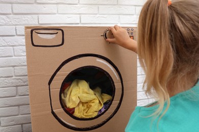 Little girl playing with toy cardboard washing machine indoors, closeup