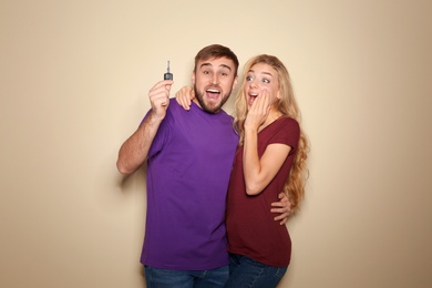 Happy young couple with car key on color background