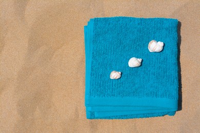 Photo of Folded soft blue beach towel with seashells on sand, flat lay. Space for text