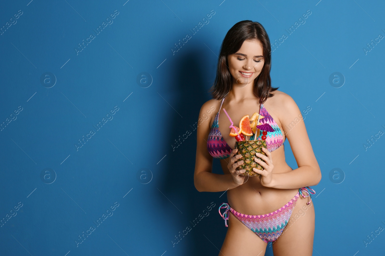 Photo of Beautiful young woman with exotic cocktail wearing bikini on blue background. Space for text