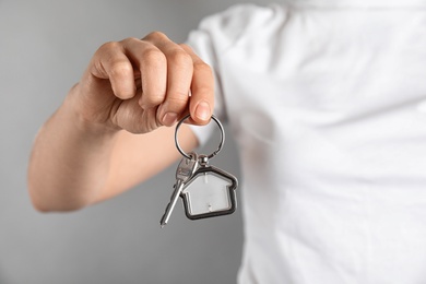 Young woman holding house key with trinket on grey background, closeup