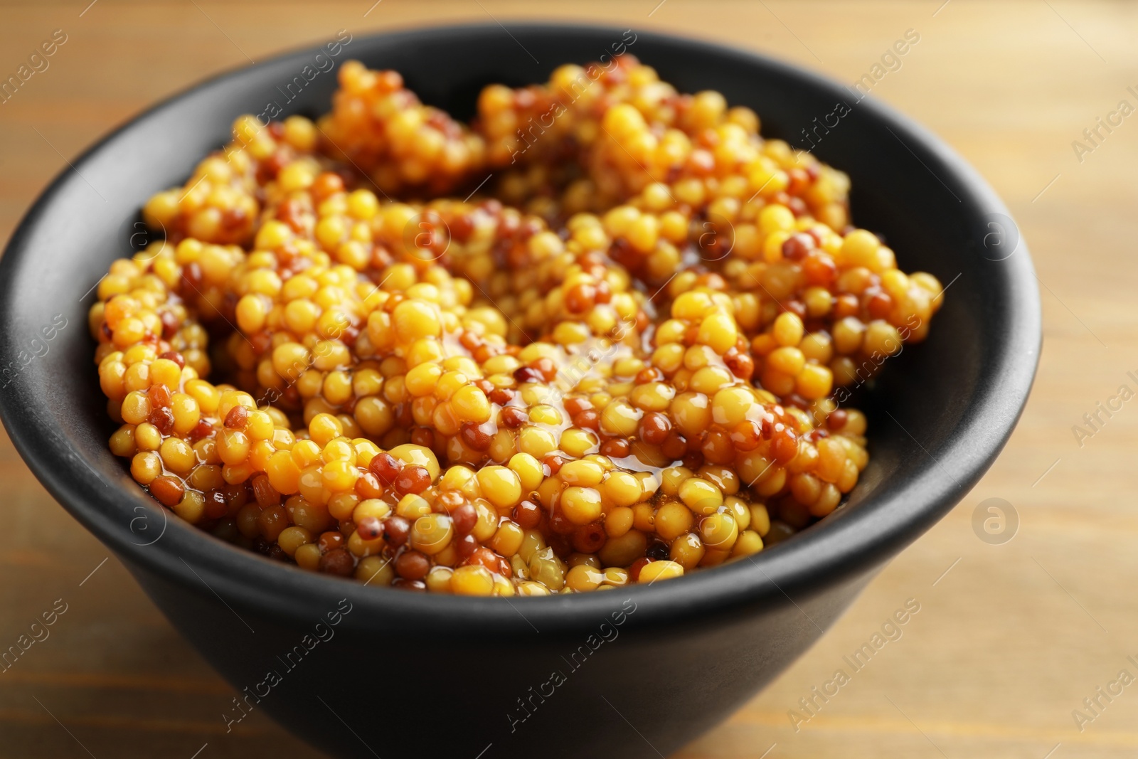 Photo of Fresh whole grain mustard in bowl on wooden table, closeup