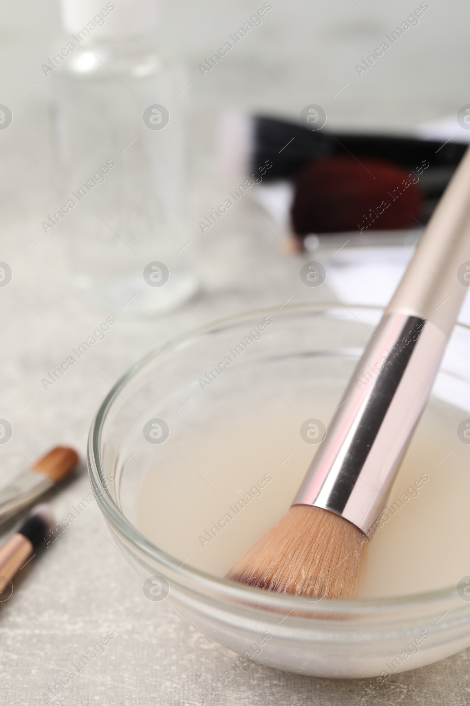 Photo of Makeup brush in bowl with cleanser on light grey table