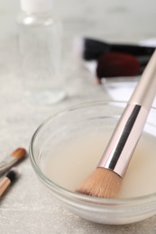 Makeup brush in bowl with cleanser on light grey table