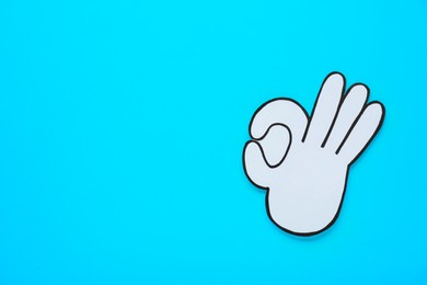 Photo of Paper cutout of okay hand gesture on light blue background, top view. Space for text