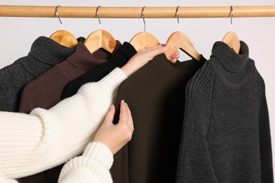 Photo of Woman taking sweater from rack on light background, closeup