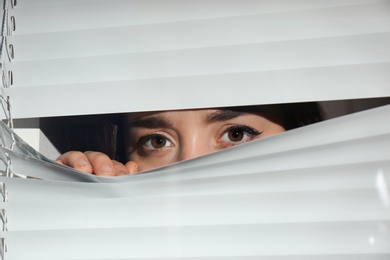 Curious woman looking through Venetian window blinds
