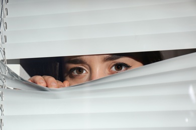 Photo of Curious woman looking through Venetian window blinds