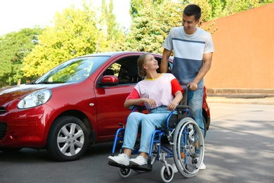 Photo of Young man with disabled woman in wheelchair near car outdoors