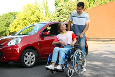 Young man with disabled woman in wheelchair near car outdoors