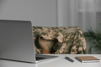 Notebook, laptop and pen on white table indoors. Military education