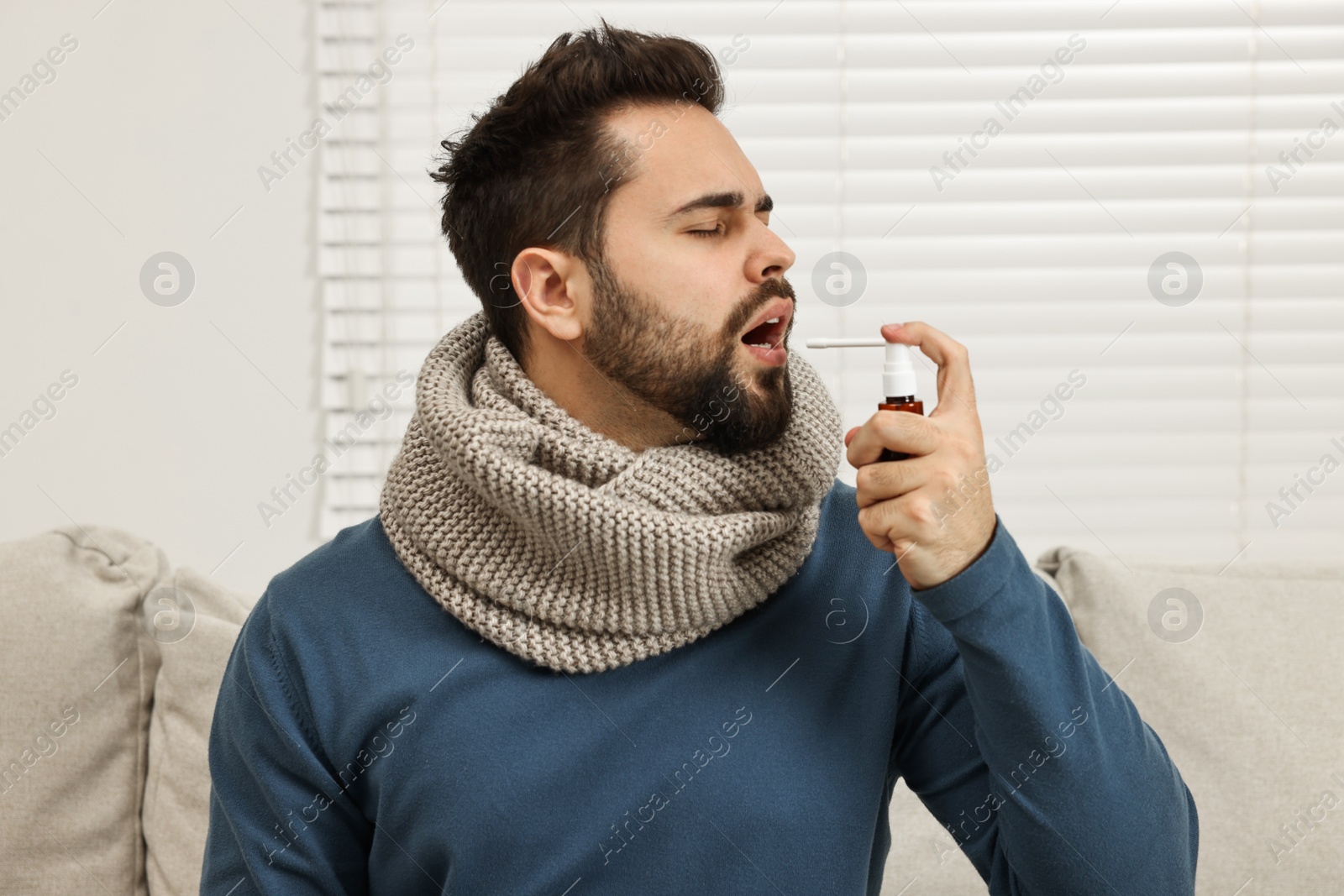 Photo of Young man with scarf using throat spray indoors