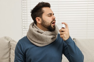 Young man with scarf using throat spray indoors