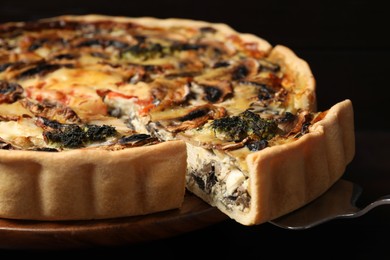 Photo of Delicious quiche with mushrooms and spatula against dark background, closeup