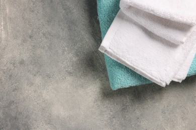 Soft folded terry towels on light gray textured background, top view. Space for text