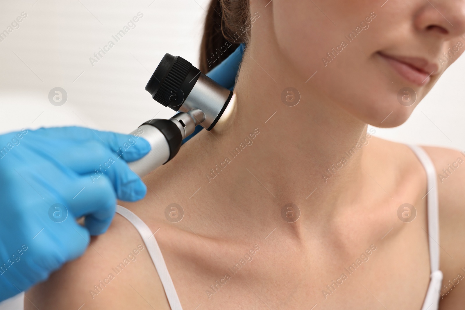 Photo of Dermatologist with dermatoscope examining patient in clinic, closeup