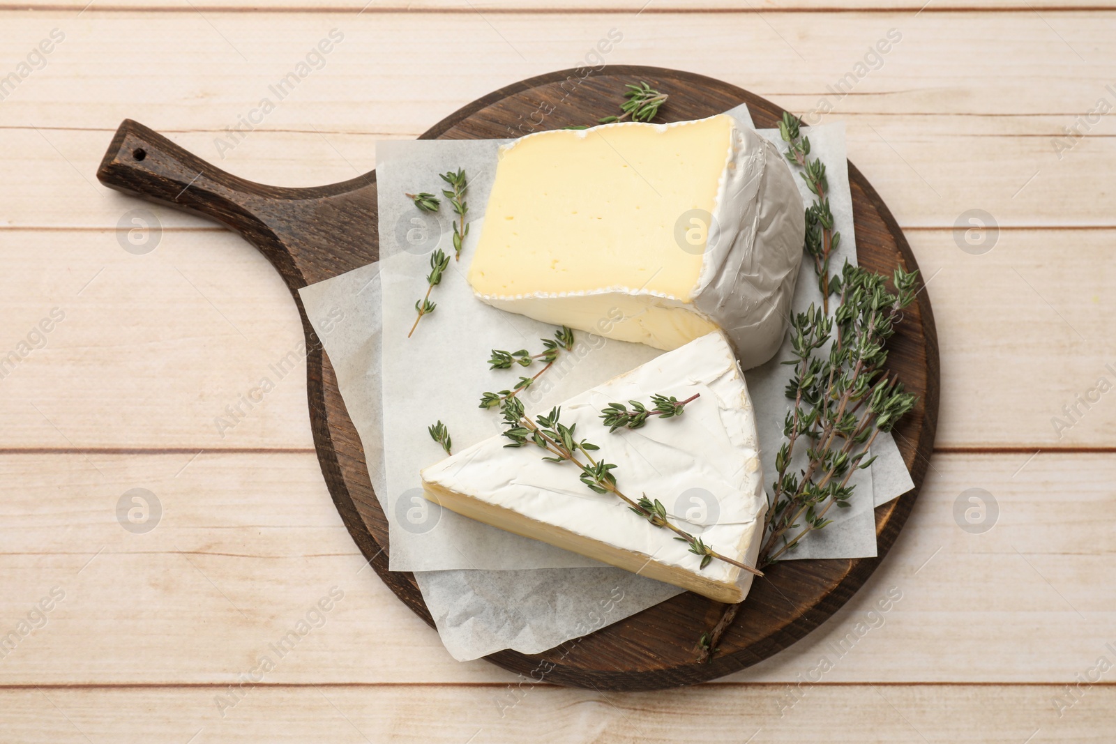 Photo of Board with pieces of tasty camembert cheese and thyme on light wooden table, top view