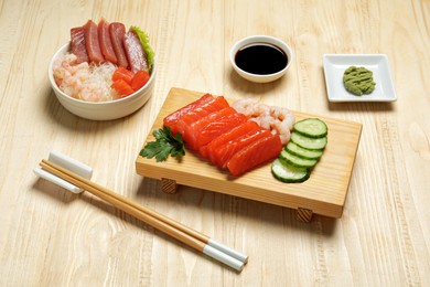 Photo of Delicious sashimi sets of salmon, shrimps and tuna served with funchosa, cucumbers, parsley, wasabi and soy sauce on wooden table