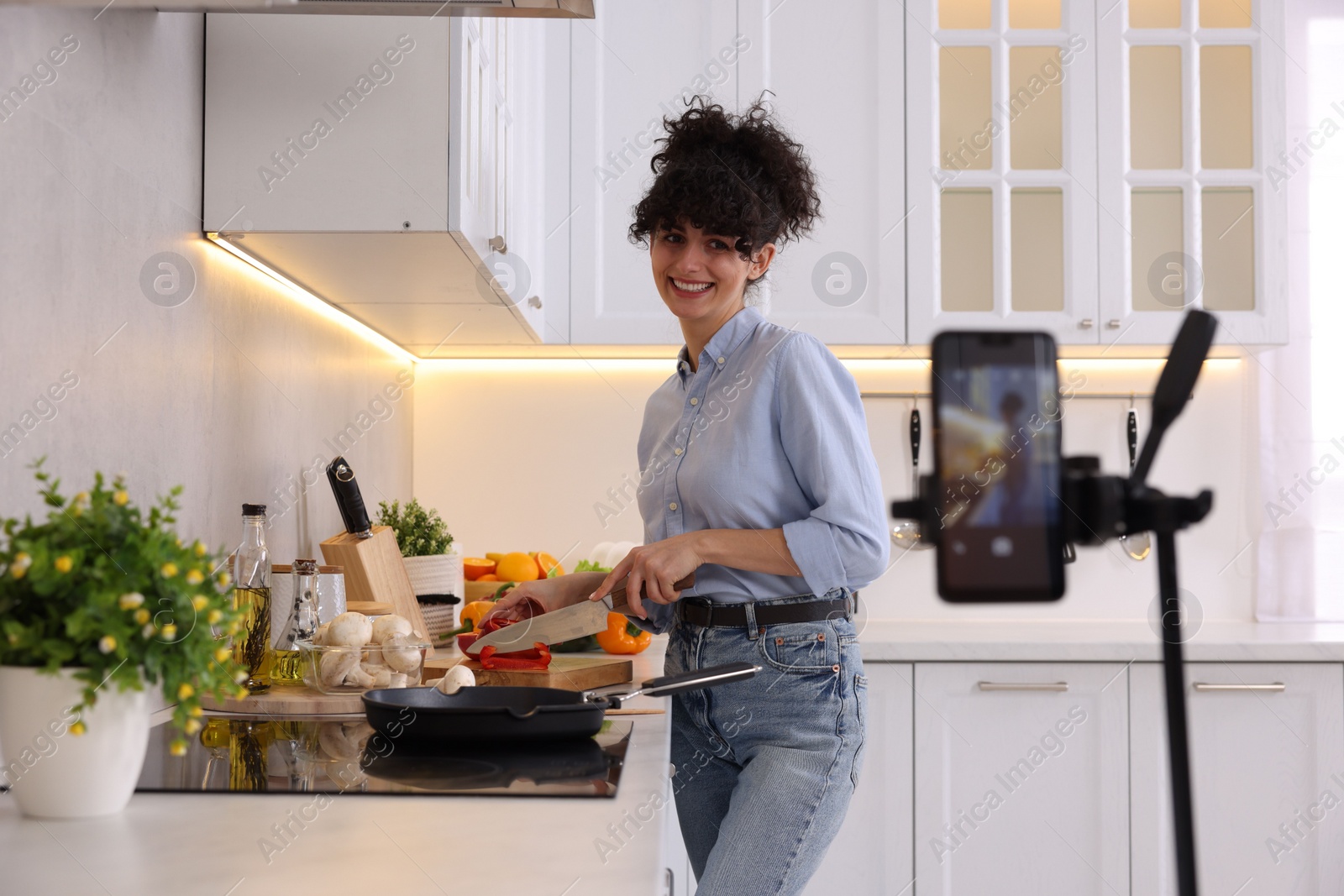 Photo of Smiling food blogger cooking while recording video in kitchen