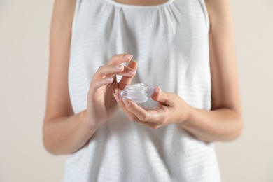 Photo of Young woman holding jar of cream on light background, closeup