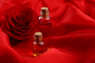 Photo of Bottles of love potion and rose flower on red fabric, space for text