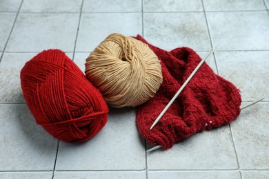 Photo of Soft woolen yarns, knitting and needles on grey tiled background
