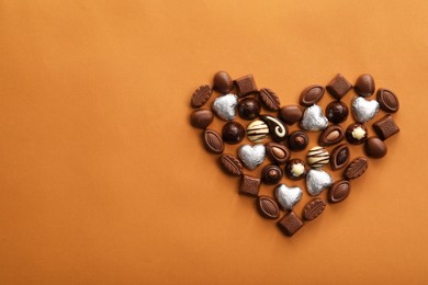 Photo of Heart made with delicious chocolate candies on brown background, top view. Space for text