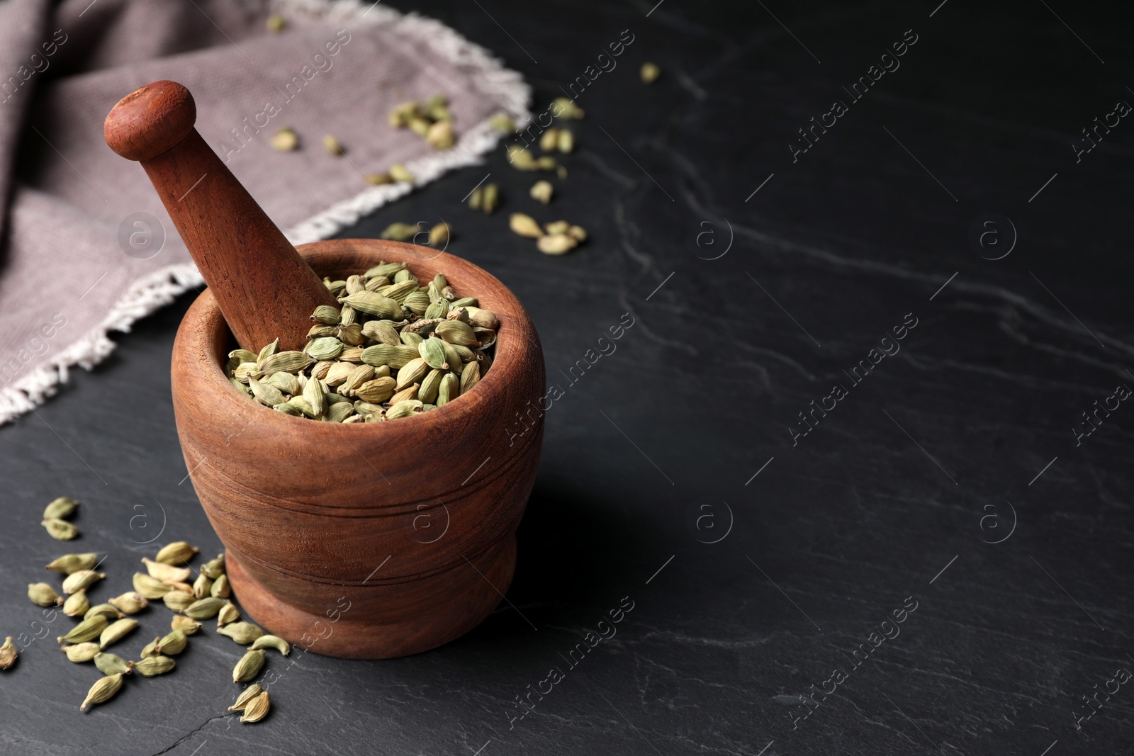 Photo of Mortar and pestle with dry cardamom pods on dark grey table, space for text