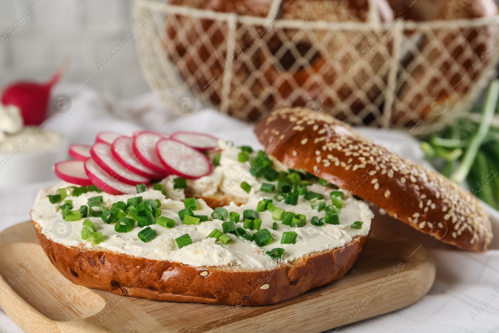 Photo of Delicious bagel with cream cheese, radish and green onion on wooden board, closeup