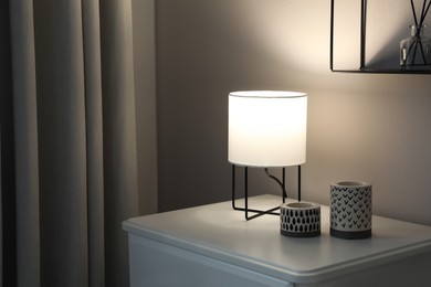 Photo of Stylish lamp and candles on white nightstand in room, space for text