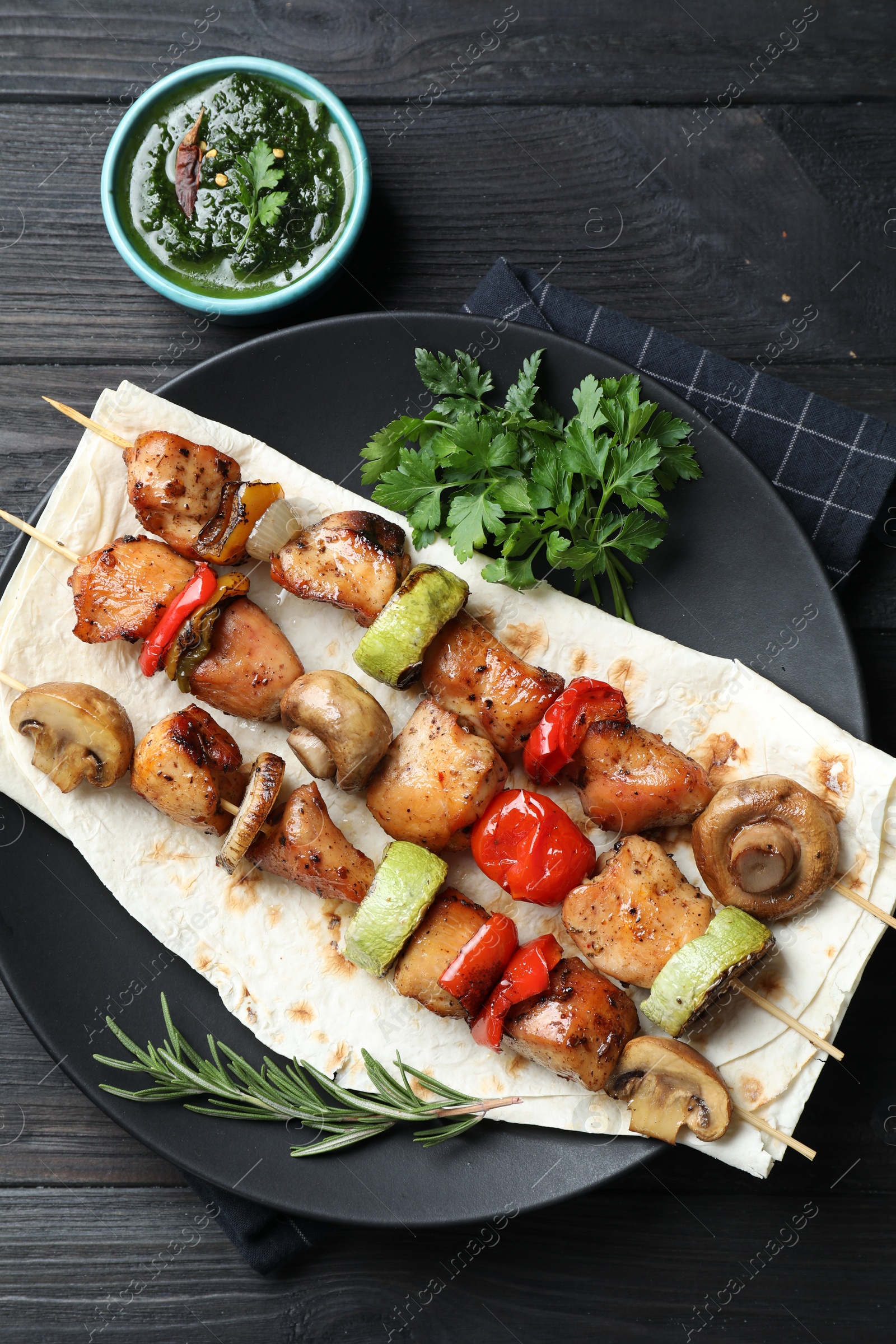 Photo of Delicious shish kebabs with vegetables served on black wooden table, flat lay