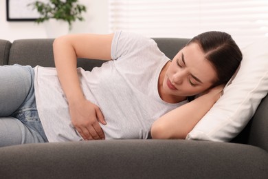 Photo of Woman suffering from abdominal pain while lying on sofa at home. Unhealthy stomach