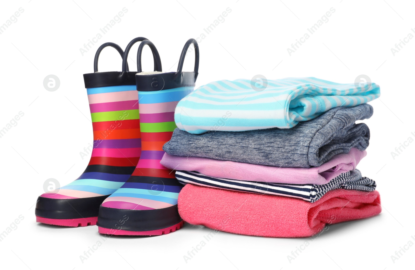 Photo of Colorful children's rubber boots and stack of clothes on white background