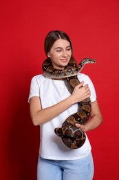 Photo of Young woman with boa constrictor on red background. Exotic pet