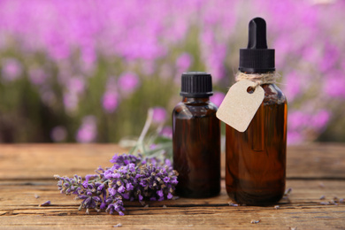 Photo of Bottles of natural essential oil and lavender flowers on wooden table, closeup. Space for text