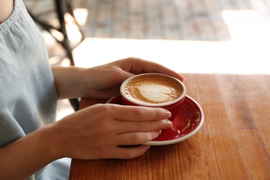 Woman with cup of fresh aromatic coffee at table, closeup