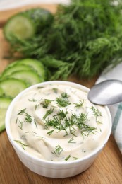 Tasty creamy dill sauce in bowl on wooden board