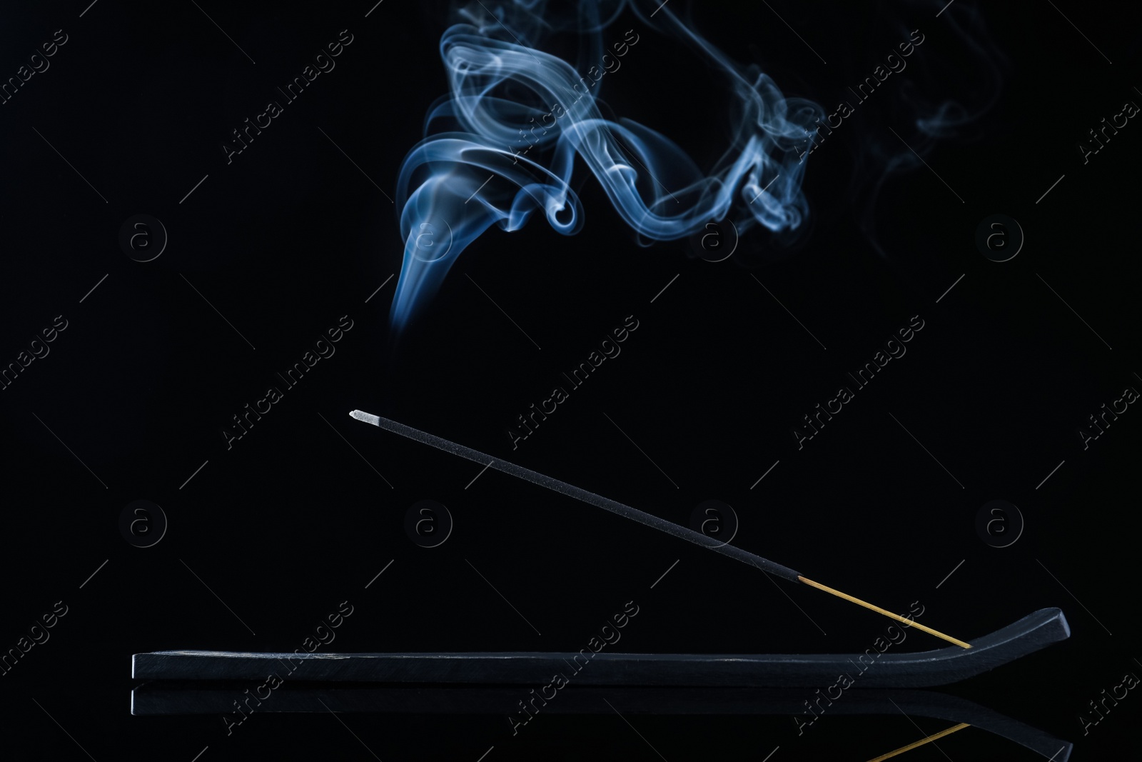 Photo of Incense stick smoldering in holder on black background