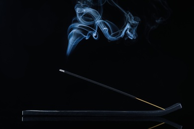 Incense stick smoldering in holder on black background