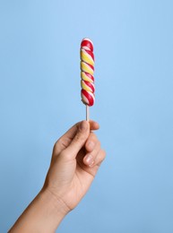 Photo of Woman holding bright tasty lollipop on light blue background, closeup