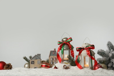 Photo of Decorative lanterns and Christmas decor on snow against light grey background