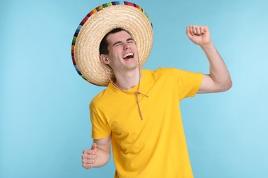 Photo of Young man in Mexican sombrero hat dancing on light blue background