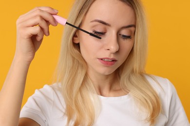 Beautiful woman applying mascara on orange background, closeup