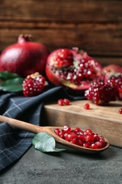 Photo of Ripe pomegranates and spoon with seeds on table against wooden background