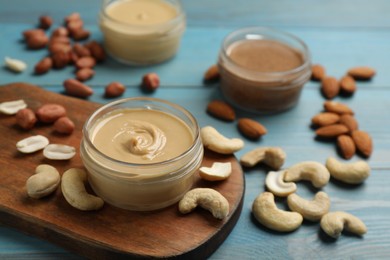 Jars with butters made of different nuts and ingredients on light blue wooden table, closeup