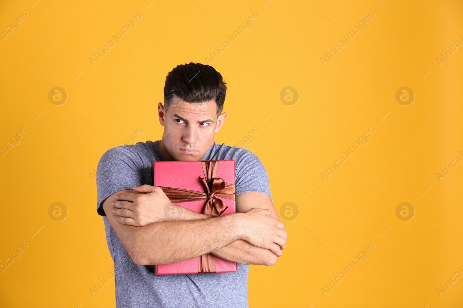 Photo of Greedy man hiding gift box on yellow background, space for text