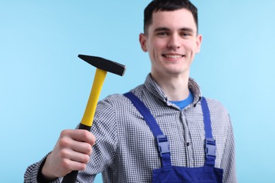 Professional repairman holding hammer on light blue background