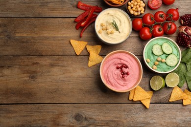 Photo of Different kinds of tasty hummus served with nachos on wooden table, flat lay. Space for text